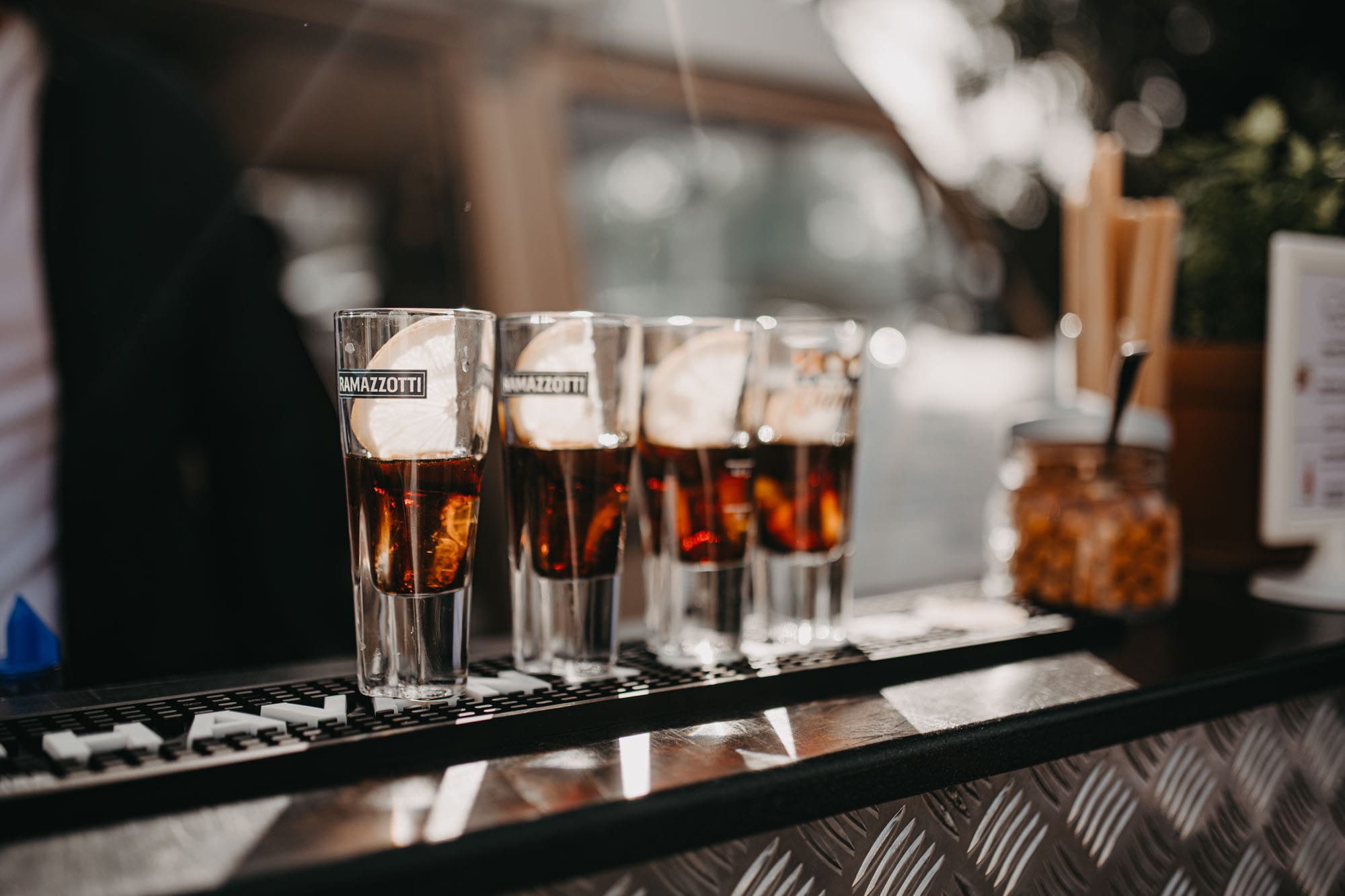 Vier gefüllte Ramazotti Gläser stehen auf der Cocktail Bar und werden von den Sonne angestrahlt.